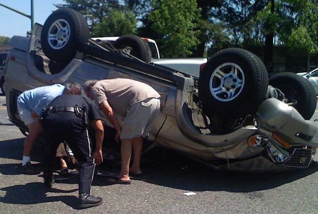 People helping person out of upside down vehicle on road.